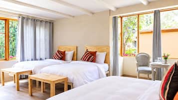 Une chambre d’hôtel avec deux lits, une table en bois, une chaise et une vue sur la verdure par les fenêtres.