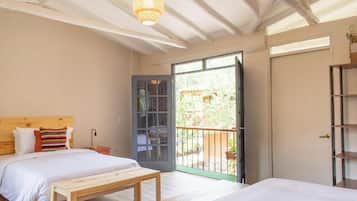 Une chambre à coucher comprenant un lit, un banc, une table de chevet et une porte donnant sur un balcon.