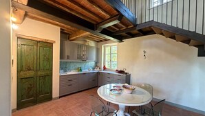 A kitchen with a round table and chairs, wooden beams on the ceiling, and a green door. - Holiday Home 'Tuscany Terroir' with Private Garden, Wi-Fi and Air Conditioning (Capannori)