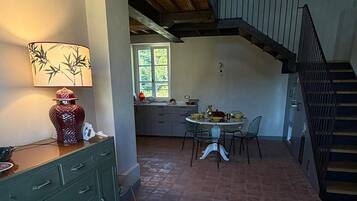 Ein geräumiger Raum mit hoher Decke und freiliegenden Holzbalken, ein Essbereich mit Tisch und Stühlen sowie eine Treppe, die zu einer oberen Ebene führt.