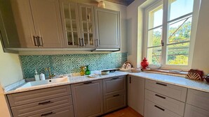 A kitchen with grey cabinets, a tiled backsplash, and a window providing a view of greenery outside. - Holiday Home 'Tuscany Terroir' with Private Garden, Wi-Fi and Air Conditioning (Capannori)