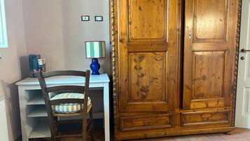 A room with a wooden wardrobe, a desk with a chair, and a lamp.