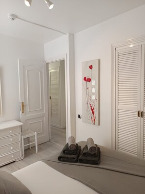 A room with a white dresser, a door, a towel rack, and a painting on the wall. - DANICO PLAYA HONDA 51/C (Playa de las Américas)