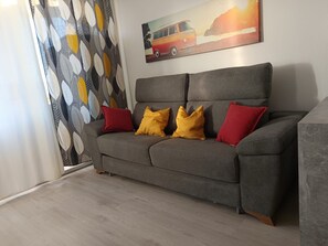 A grey sofa with red and yellow cushions, a painting of a van on the wall, and patterned curtains. - DANICO PLAYA HONDA 51/C (Playa de las Américas)