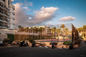 A modern building with a tennis court, surrounded by palm trees and parked scooters. - DANICO PLAYA HONDA 51/C (Playa de las Américas)