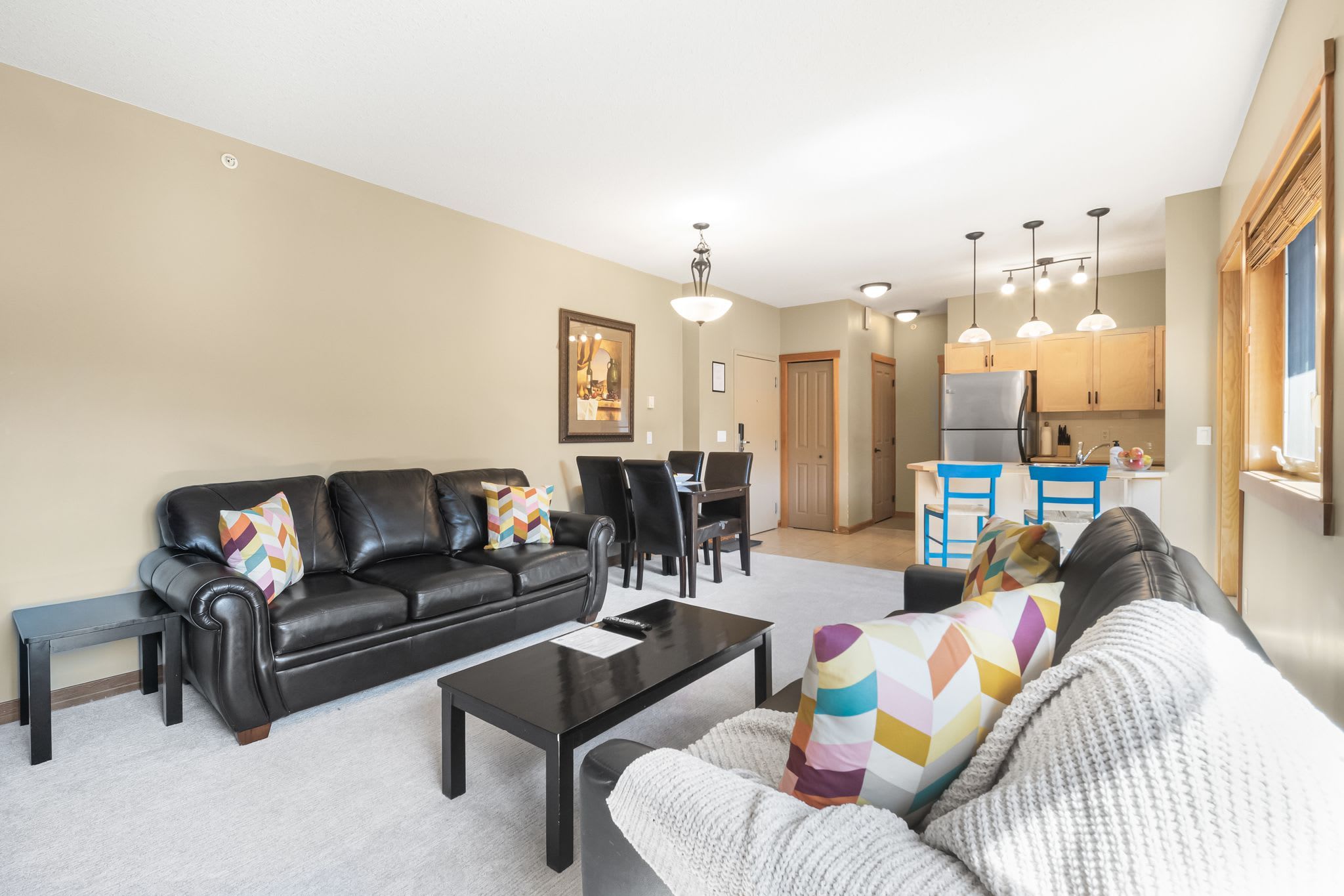 A living room with a black leather sofa, a white sofa, a coffee table, and a dining area with chairs and a table.