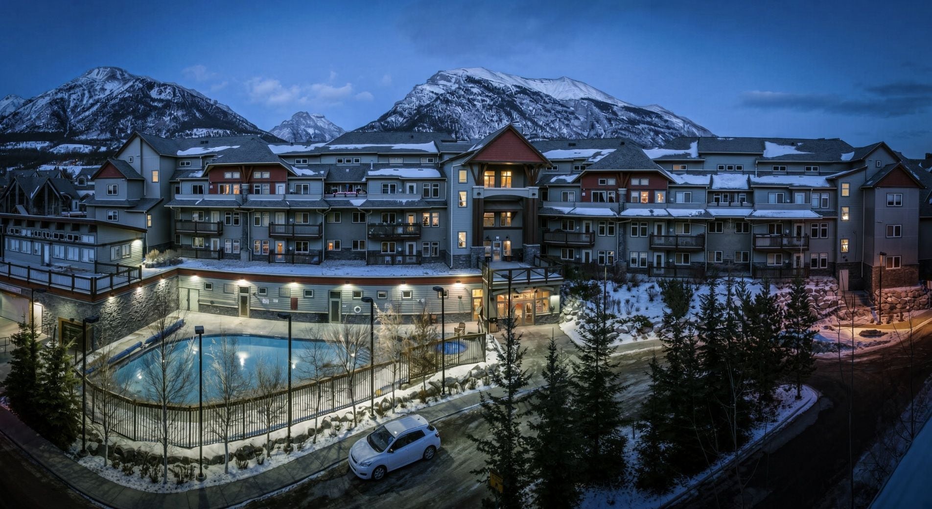 A multi-story hotel with a pool area, surrounded by snow-covered mountains.