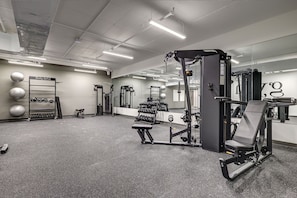 Een sportschool met diverse fitnessapparaten, een spiegelwand en een dumbbellsrek.