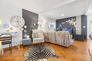 Una sala de estar moderna con un sofá, un sillón, alfombra de cebra y televisión.