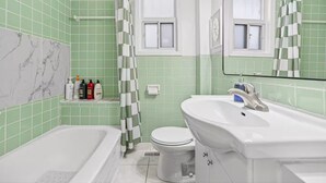 A bathroom with a bathtub, toilet, and sink, featuring green tiles and a marble accent wall. - Bright & Cozy 2BR Stay in Toronto Near Transit (Toronto)