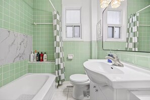 Un baño con bañera, inodoro y lavamanos, con azulejos verdes y una pared de acento de mármol.