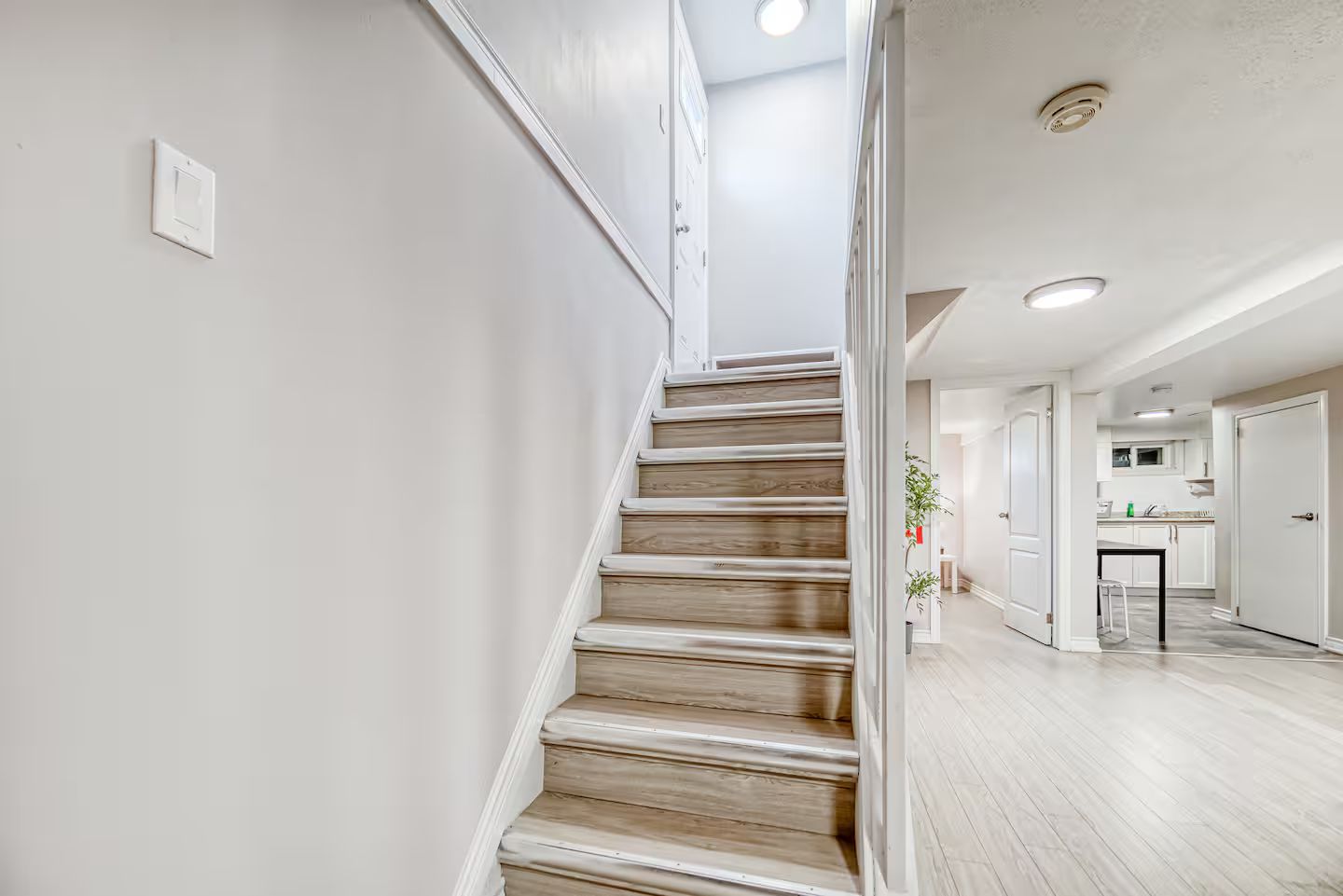 A staircase leading to a modern kitchen area with white walls and wooden flooring.