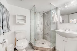 Ein modernes Badezimmer mit einer gläsernen Duschkabine, einer weißen Toilette, einem Waschbecken mit Spiegel und einem Handtuchhalter.