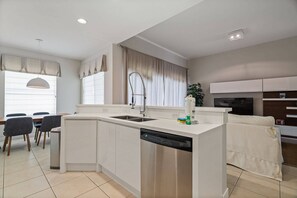 A modern kitchen with a dishwasher, a dining area with chairs, a sofa, and a TV. - Windsor Hills 5BR Home Near Disney Parks (Kissimmee)