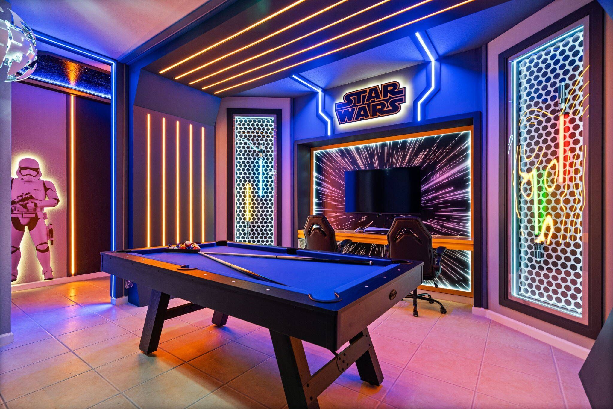 A pool table in a room with Star Wars decor, including a large screen and a neon sign.