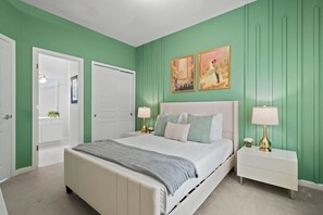 A bedroom with a bed, two bedside tables, a nightstand, a door, and two framed pictures on the wall. - Windsor Hills 5BR Home Near Disney Parks (Kissimmee)