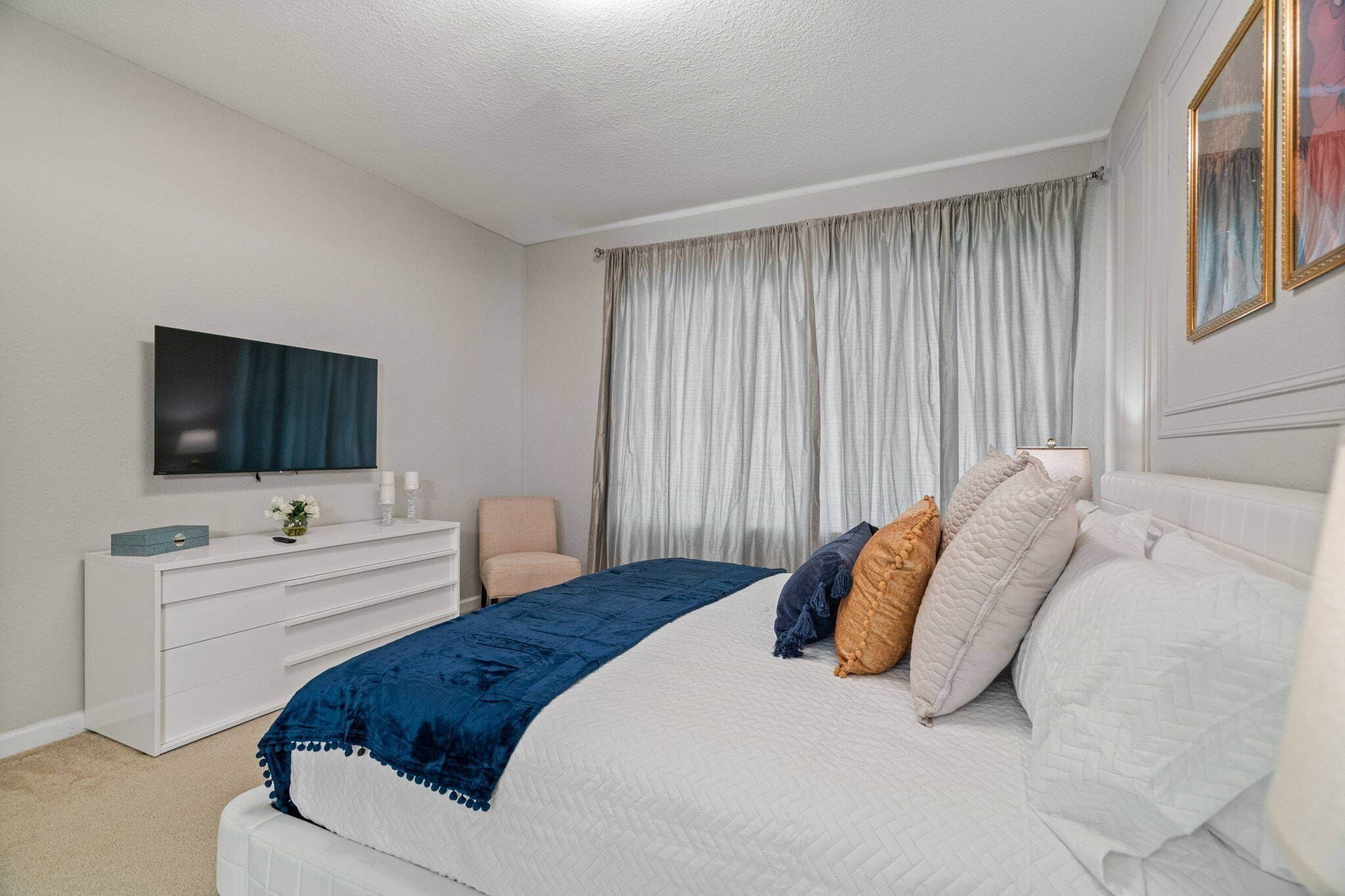 A bedroom with a bed, a dresser, a television, and a window with curtains.