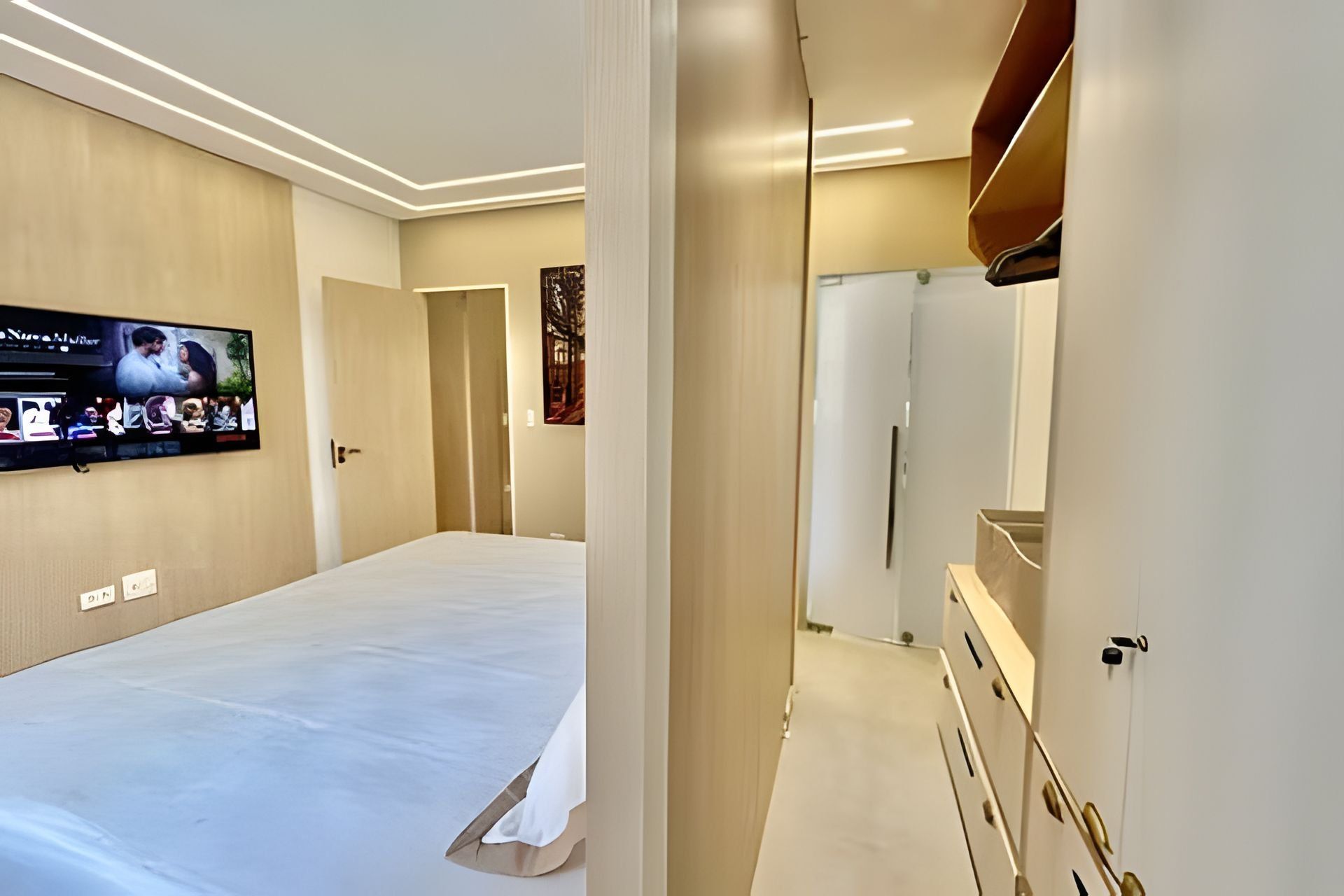 A hotel room with a large bed, a flat-screen TV mounted on the wall, and a modern design with neutral colors.