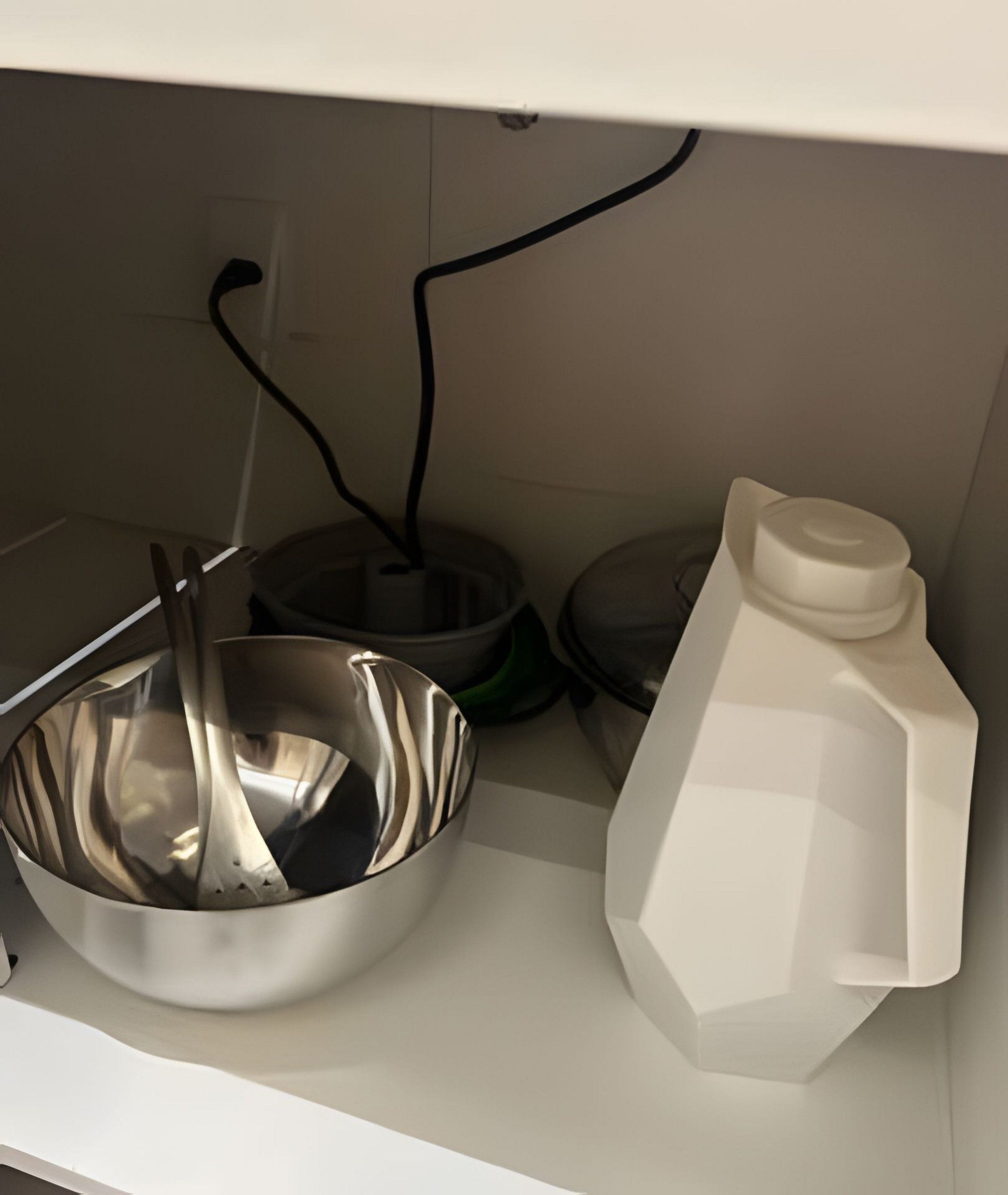 Uma cozinha com uma tigela de mistura de aço inoxidável, um recipiente de plástico branco e um cabo elétrico preto.