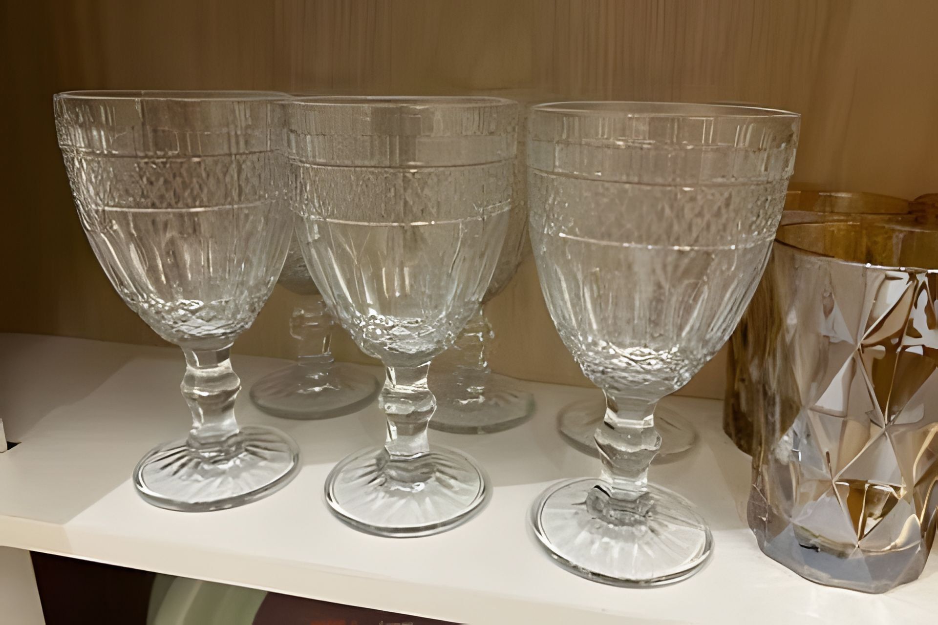 Tres copas de cristal transparentes sobre un estante blanco.