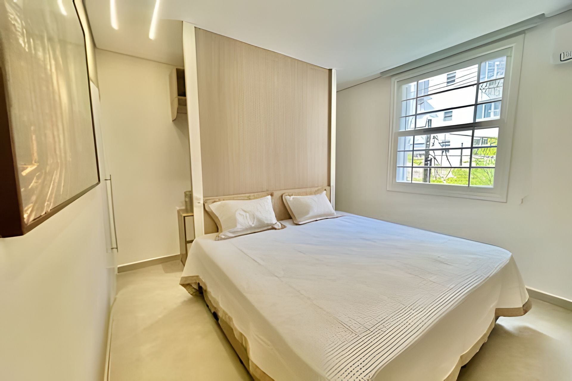 A bedroom with a large bed, a wooden headboard, a window with a view of greenery, and a door leading to another room.