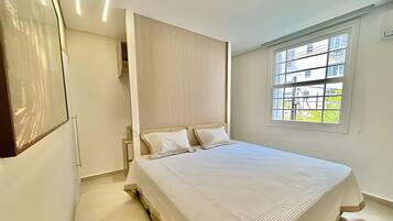 A bedroom with a large bed, a wooden headboard, a window with a view of greenery, and a door leading to another room.