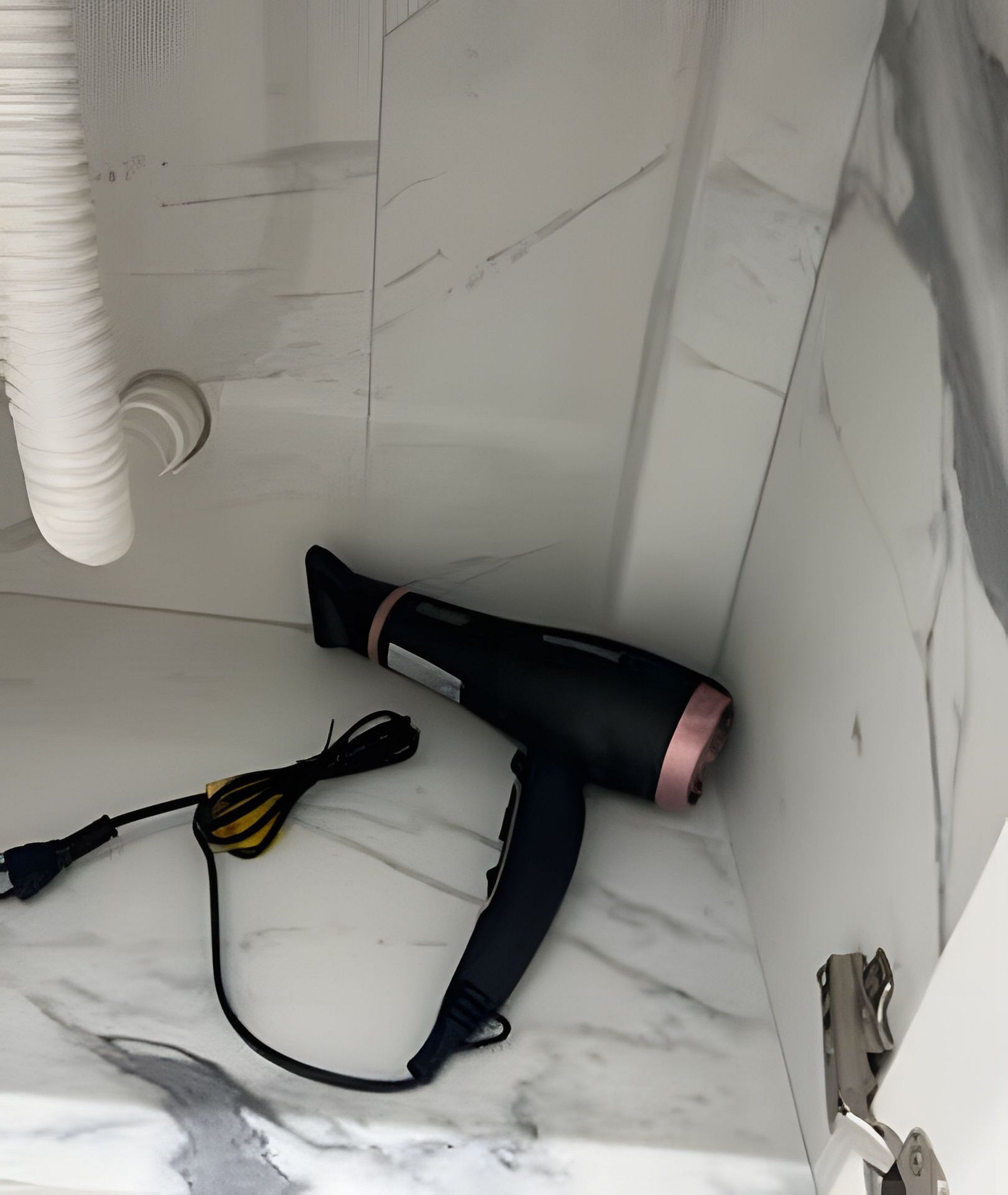A bathroom with a white marble floor, a black and pink hairdryer, and a black and yellow hairbrush.