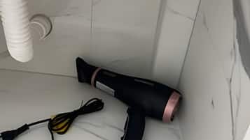 A bathroom with a white marble floor, a black and pink hairdryer, and a black and yellow hairbrush.