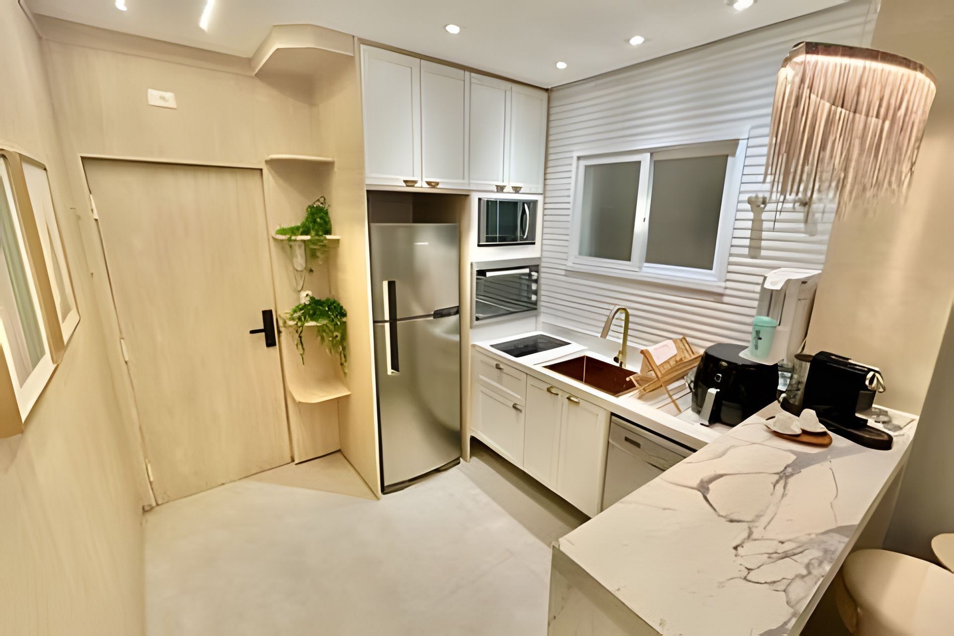 A modern kitchen with white cabinetry, a built-in oven, a stainless steel refrigerator, and a marble countertop.
