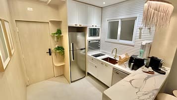Una cocina moderna con armarios blancos, horno empotrado, refrigerador de acero inoxidable y encimera de mármol.