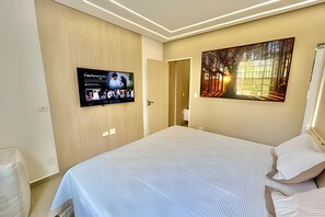 Habitación de hotel con una cama grande, un televisor de pantalla plana en la pared y un cuadro con una escena de bosque.