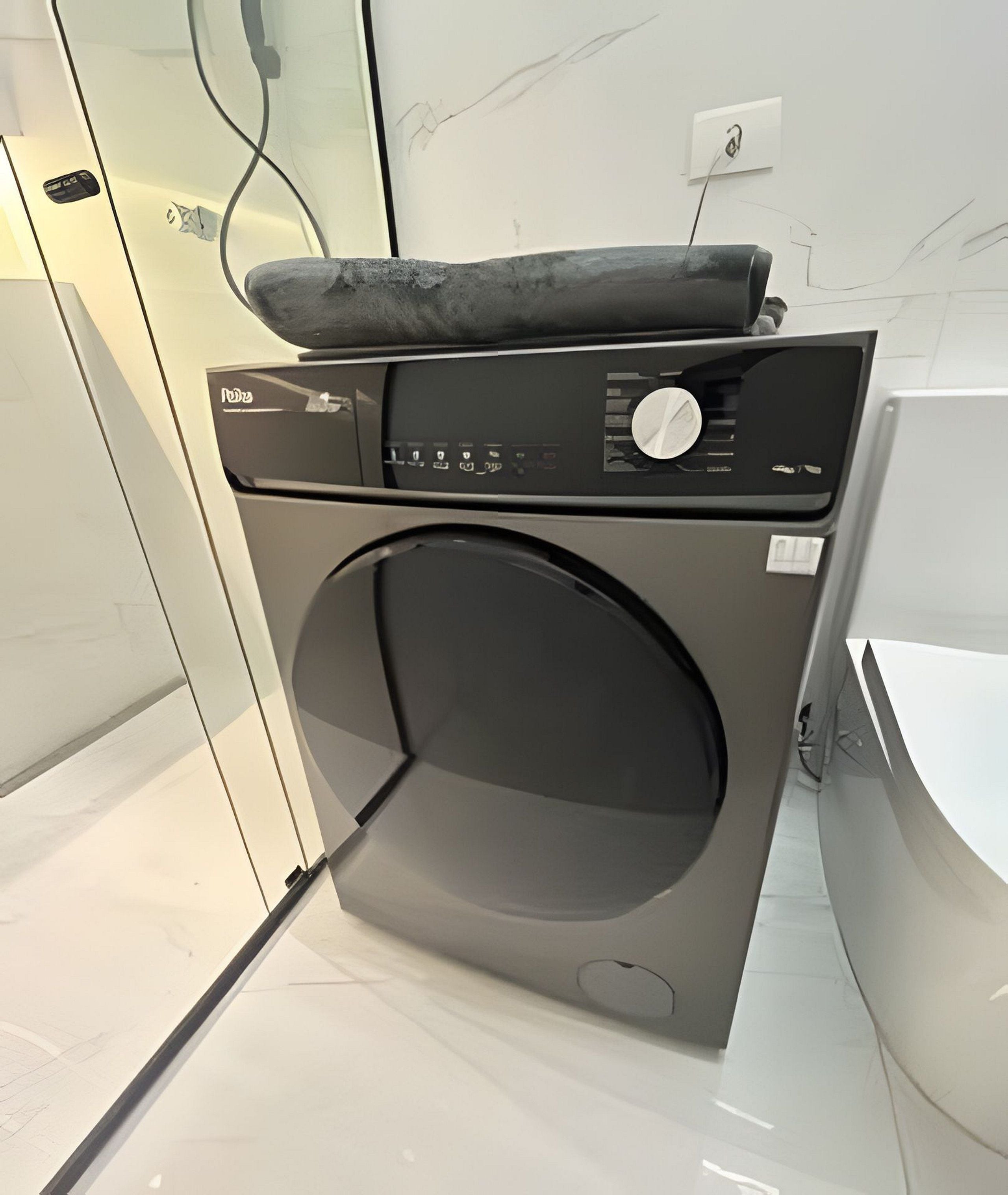 A modern, compact washing machine in a clean, minimalist bathroom with a white marble backsplash and a visible electrical outlet.