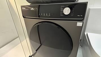 A modern, compact washing machine in a clean, minimalist bathroom with a white marble backsplash and a visible electrical outlet.