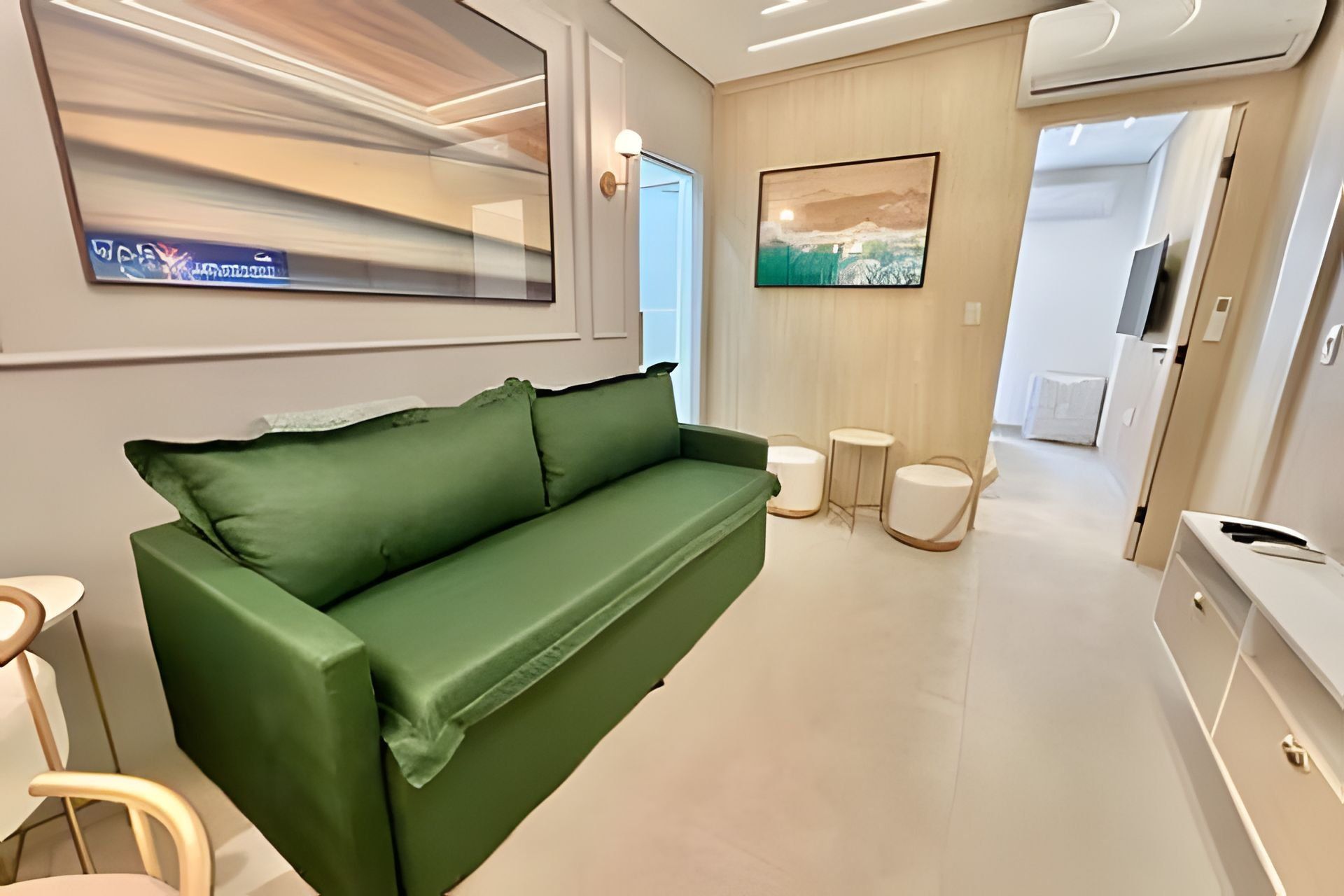 Un área de estar moderna con un sofá verde, un televisor de pantalla plana, un cuadro y una pequeña mesa redonda.