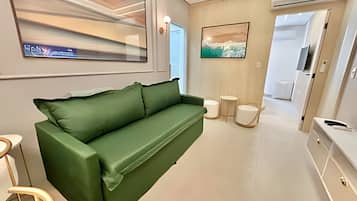 Un área de estar moderna con un sofá verde, un televisor de pantalla plana, un cuadro y una pequeña mesa redonda.