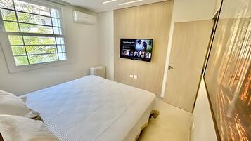 A bedroom with a bed, a TV mounted on the wall, and a window with a view of trees.
