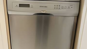 Un lavavajillas de acero inoxidable en una cocina con encimera color beige y armarios blancos.