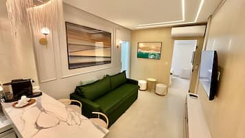 Una sala de estar moderna con un sofá verde, una máquina de café, una encimera de mármol y un televisor montado en la pared.