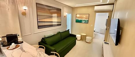 A modern living room with a green sofa, a coffee machine, a marble countertop, and a TV mounted on the wall.