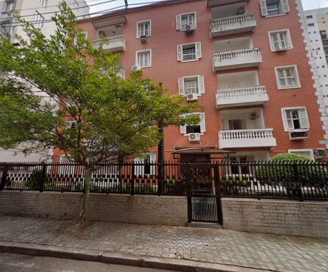 Un edificio de ladrillo de varios pisos con balcones, una acera pavimentada y una valla metálica.