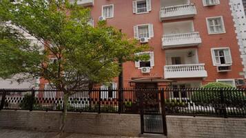 Un edificio de ladrillo de varios pisos con balcones, una acera pavimentada y una valla metálica.