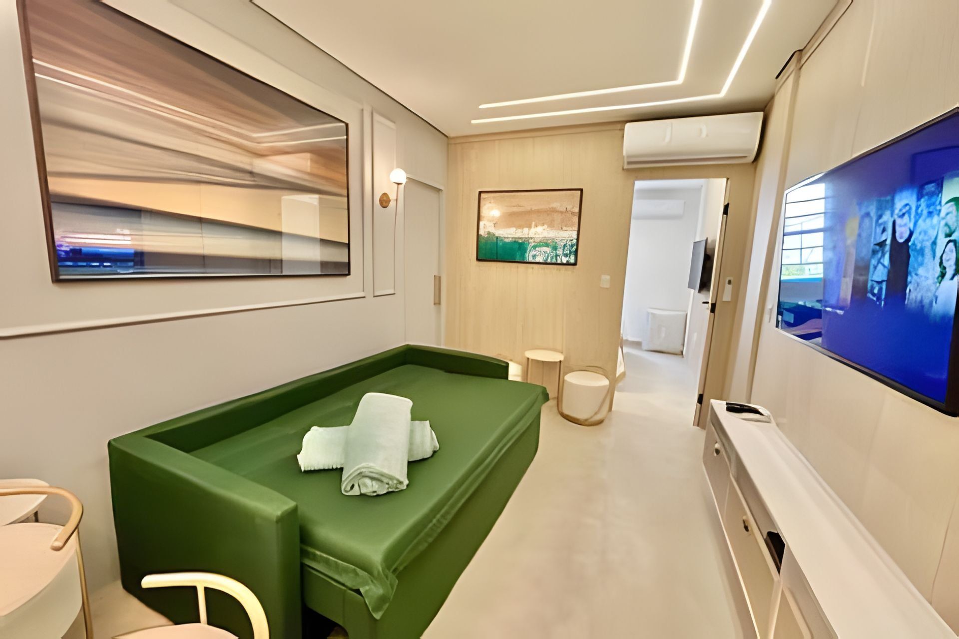 A modern hotel room with a green sofa, a TV, and a painting on the wall.