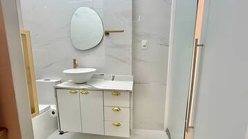 Un baño moderno con tocador blanco, pomos dorados, espejo redondo y lavamanos blanco.