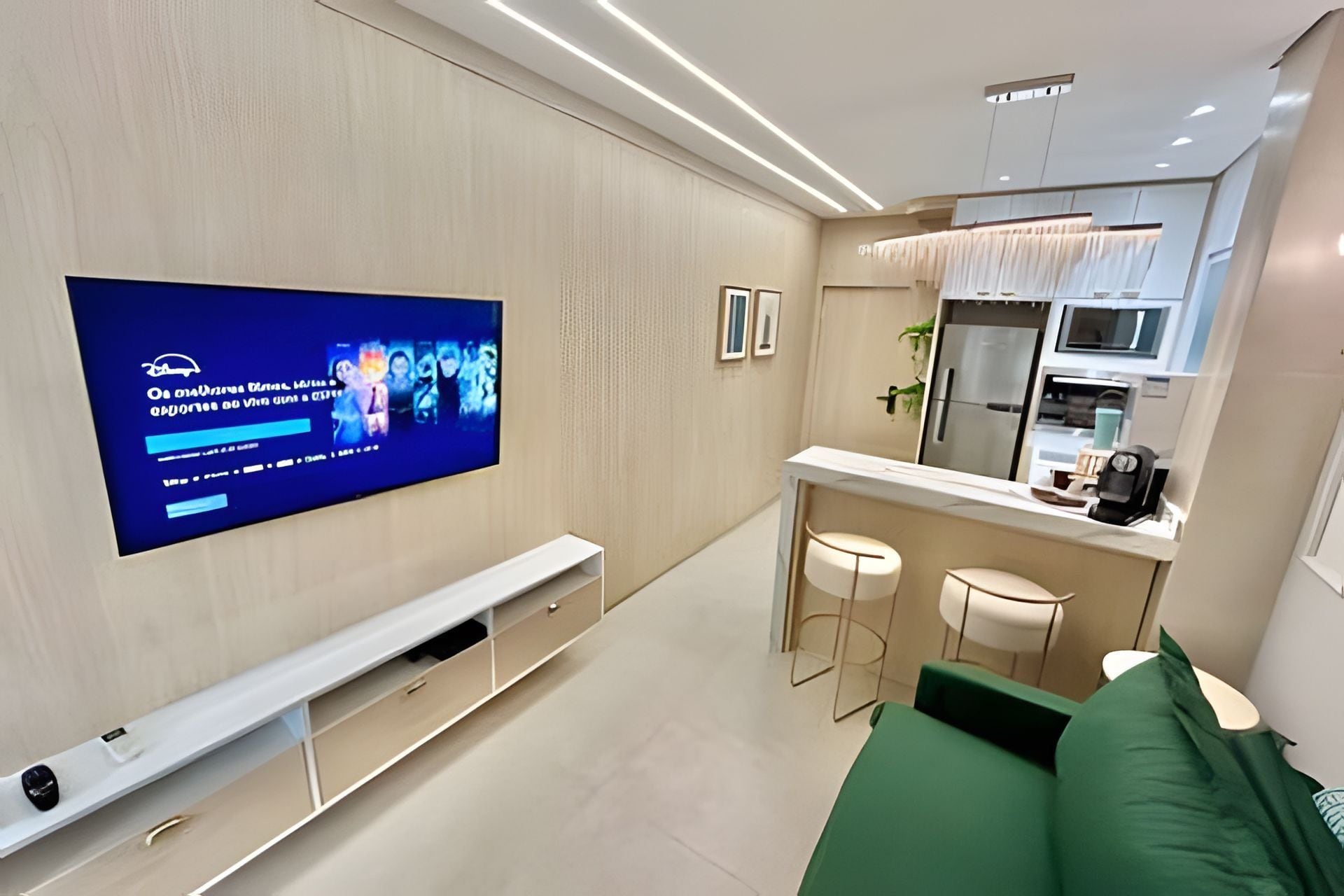Una sala de estar moderna con un televisor de pantalla plana en la pared, un sofá verde y una cocina con refrigerador y microondas.
