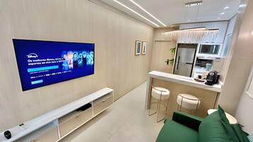 Una sala de estar moderna con un televisor de pantalla plana en la pared, un sofá verde y una cocina con refrigerador y microondas.