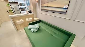 A modern bathroom with a green vanity, a sink, and a mirror. There are two stools and a towel rack.