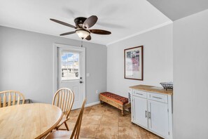 Ein Zimmer mit Esstisch, Stühlen, einer Bank, einem Schrank, einem Deckenventilator und einer Tür mit Fenster.