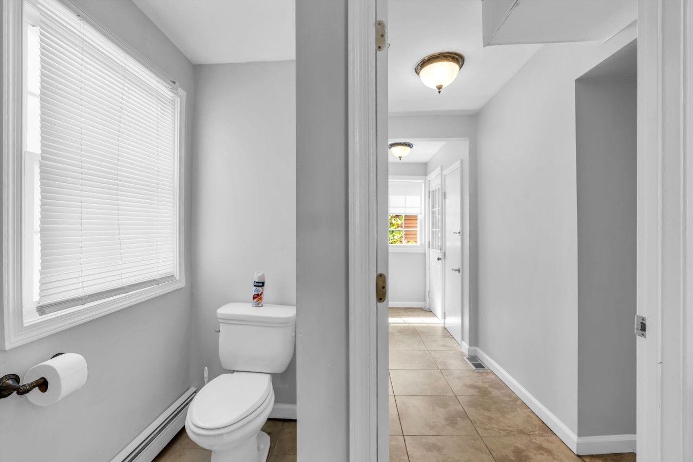 A bathroom with a toilet, a roll of toilet paper, and a window with blinds.