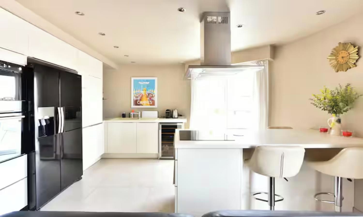 A modern kitchen with a central island, stainless steel appliances, and a decorative clock on the wall.