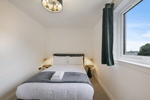 A bedroom with a bed, bedside lamps, a window with curtains, and a ceiling light fixture. - Spital Lodge - Grampian Lettings (Aberdeen)
